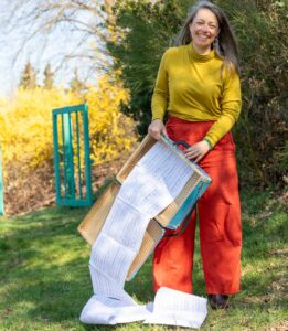 Anna Stijohann steht mit einem geöffneten Koffer im Garten, aus dem Noteblätter quillen