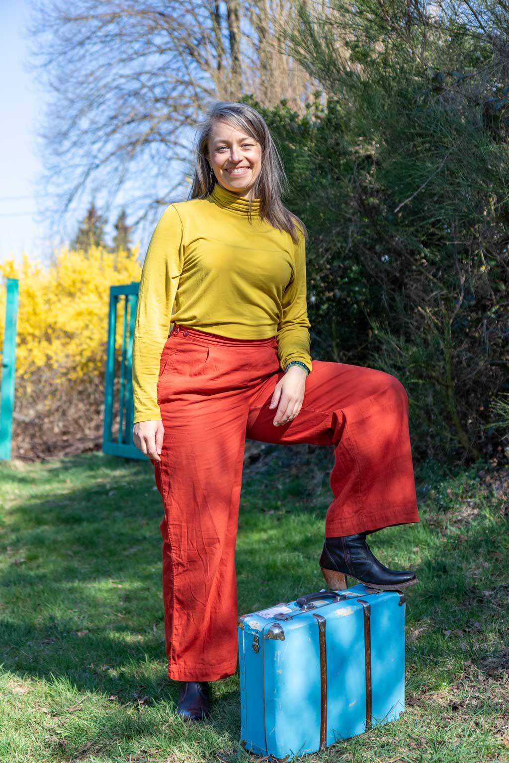Anna Stijohann im Garten, mit einem Fuß auf einem Koffer.